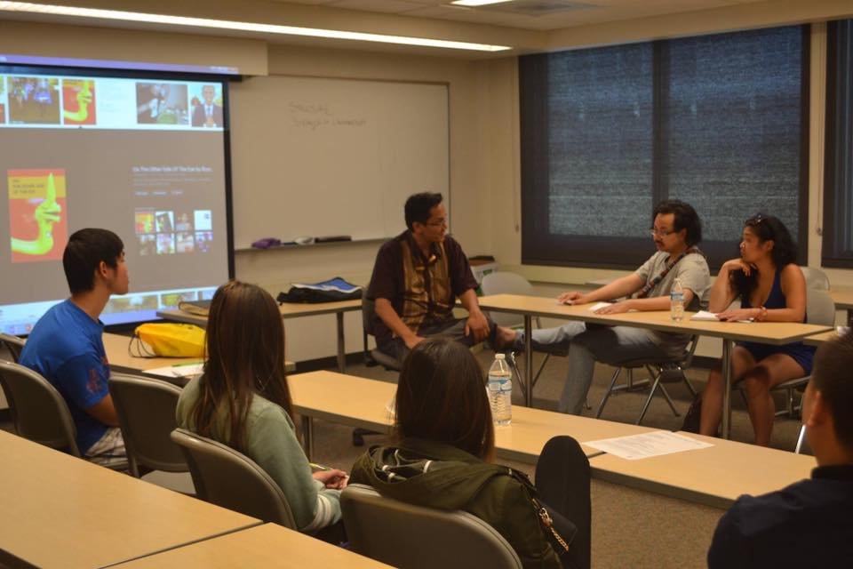 Four panelists lead a discussion with students in a classroom, with a slide of book covers projected behind them