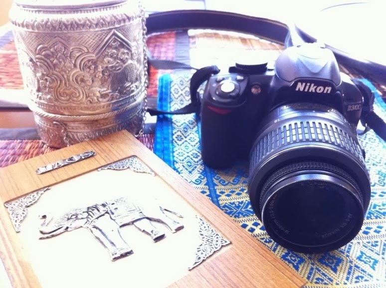 An embossed Lao silver container, a silver elephant plaque, and a Nikon camera resting on a Lao woven textile
